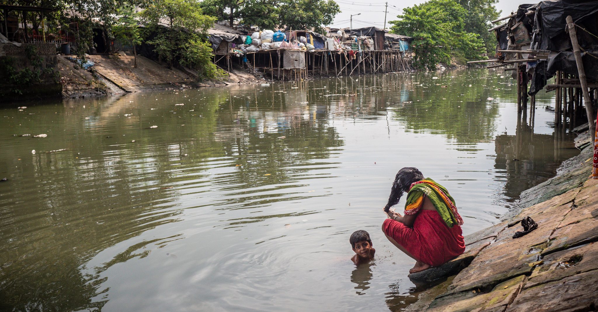 Eine Frau wäscht sich die Haare im Kanal im Slum Kolkata Station und ein Junge badet im Wasser.